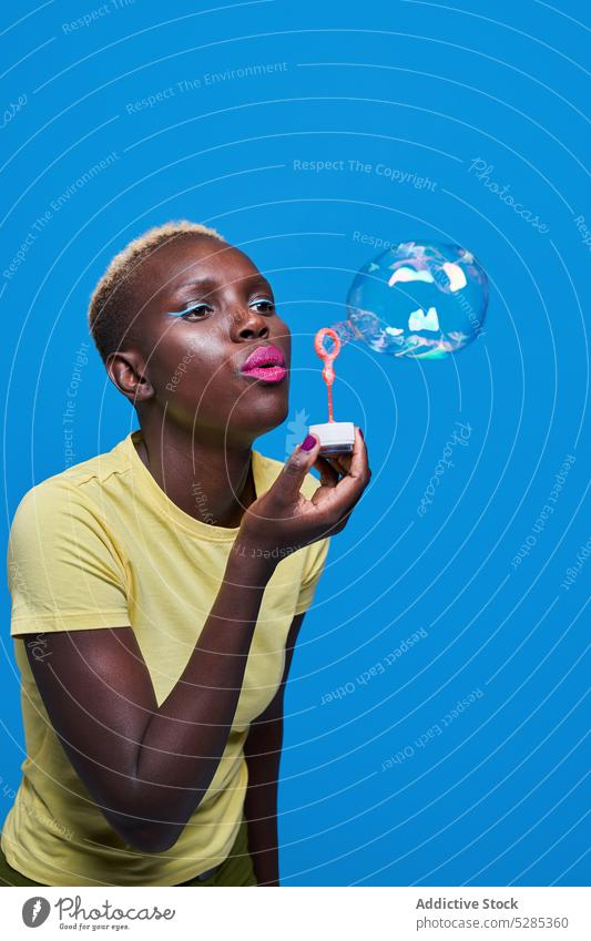 Delighted black woman blowing bubbles in studio makeup soap bubble style colorful trendy bright female african american vivid joy ethnic fashion vibrant