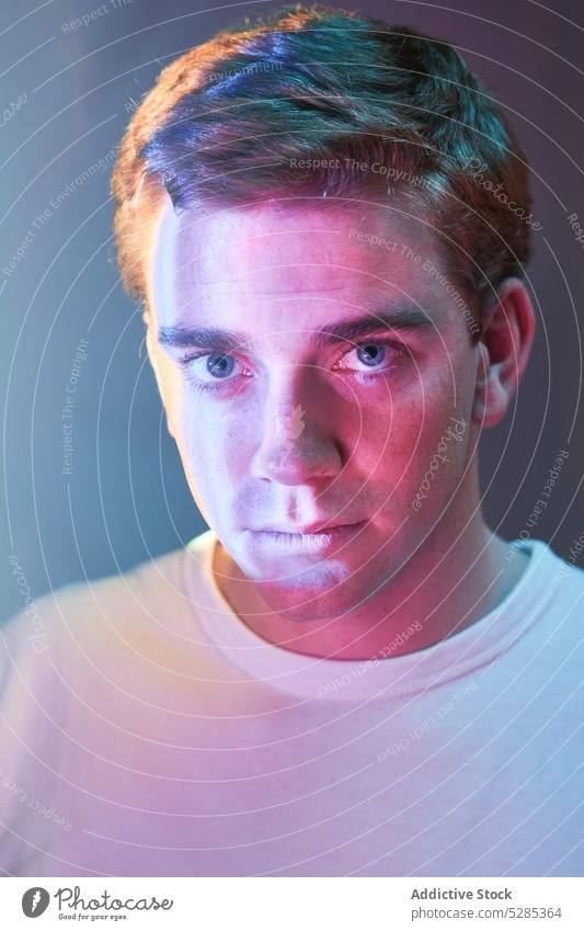 Serious man looking at camera in studio neon calm portrait appearance white shirt light serious t shirt male young confident individuality short hair style