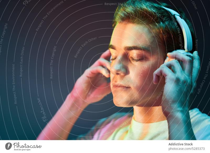 Man listening to music in headphones man neon relax wireless calm illuminate eyes closed male young sound song modern audio casual glow gadget device cool