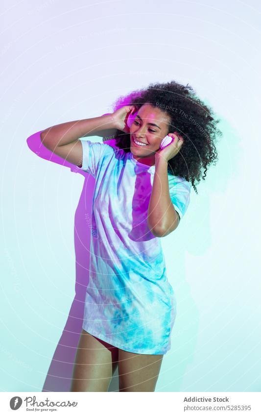 Happy black woman dancing in studio dance smile cheerful style neon headphones music happy positive young curly hair female ethnic african american trendy party