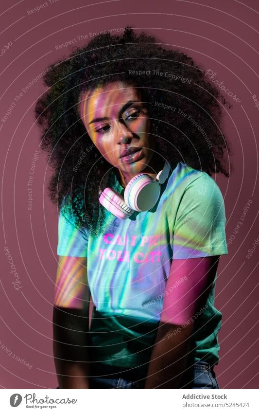 Thoughtful black woman with headphones in neon pensive thoughtful trendy light serious reflection style female young ethnic curly hair illuminate
