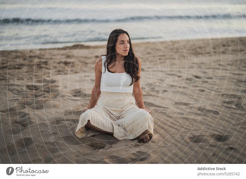 Relaxed young Hispanic lady sitting on sandy seashore with crossed legs woman beach rest holiday tourist vacation legs crossed recreation alone enjoy relax