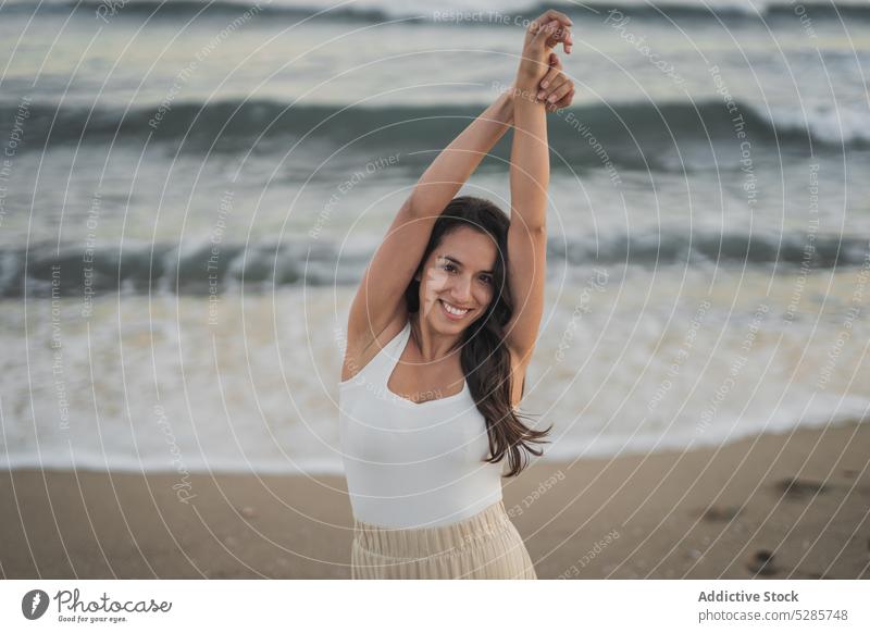 Content young Hispanic woman dancing on sandy beach dance sunset arms raised positive sea perform confident feminine carefree cheerful female outstretched arms