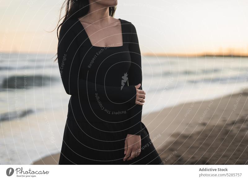Self assured anonymous ethnic lady standing on sandy seashore woman beach tourist sunset vacation confident feminine female young hispanic brunette dress