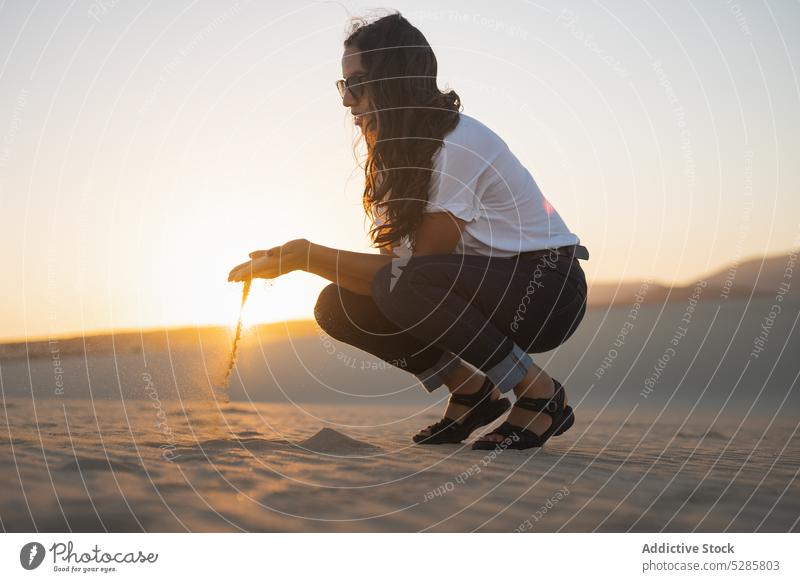 Woman playing with sand woman beach sunset summer happy sea coast female vacation sunglasses casual relax bali rest evening joy holiday weekend carefree sundown