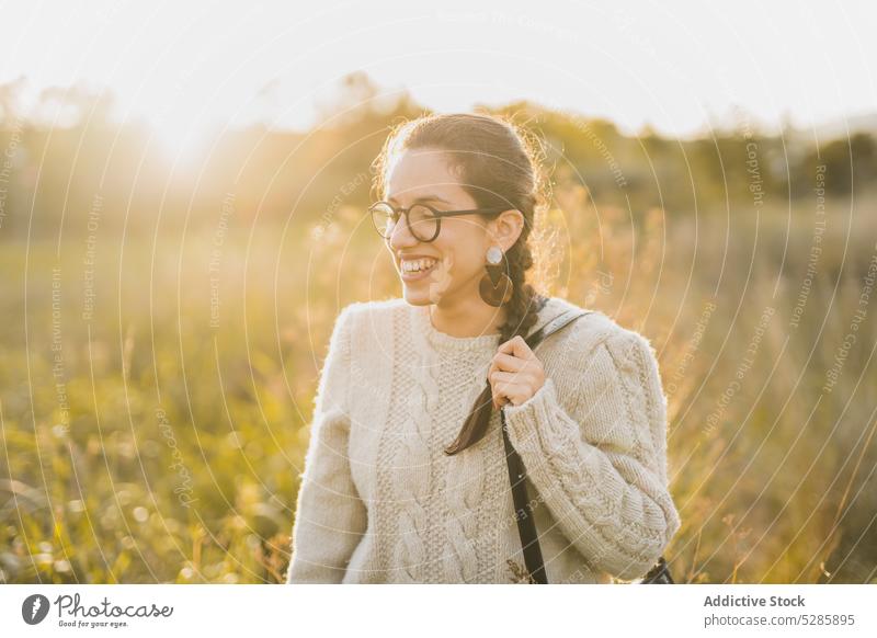 Cheerful woman enjoying time in countryside smile touch hair sunset field nature happy cheerful relax female young eyeglasses sweater meadow positive summer