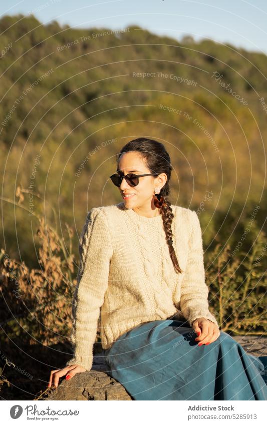 Relaxed woman resting on stone trendy countryside relax positive style smile nature rural female young ethnic summer sunglasses cheerful happy confident content