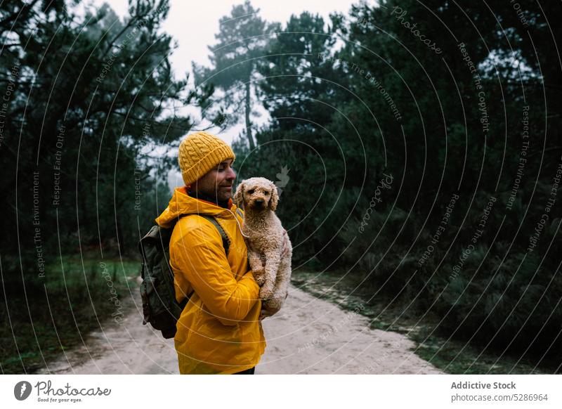 Backpacker holding puppy in autumn forest man owner dog pet happy affection smile bonding companion woods male woodland overcast delight glad active weather guy