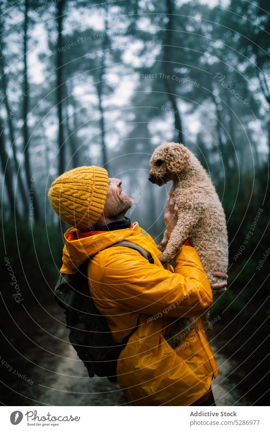 Backpacker holding puppy in autumn forest man owner dog pet happy affection smile bonding companion woods male woodland overcast delight glad active weather guy