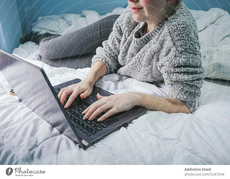 Anonymous female freelancer using computer on bed woman laptop self employed browsing independent typing chat project gadget online connection bedroom lady