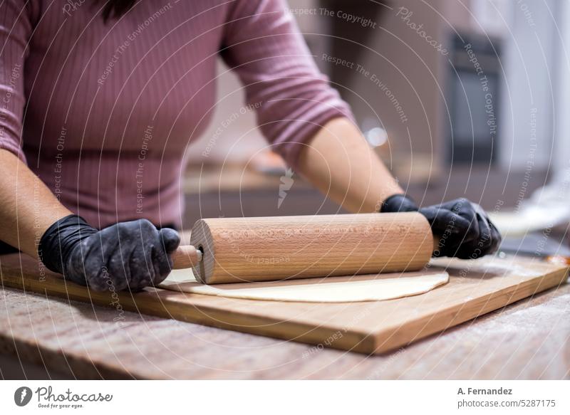Detail of a woman kneading a pizza dough with a wooden rolling pin on a kitchen counter while wearing black gloves pizza maker pizza making Dough dough roller