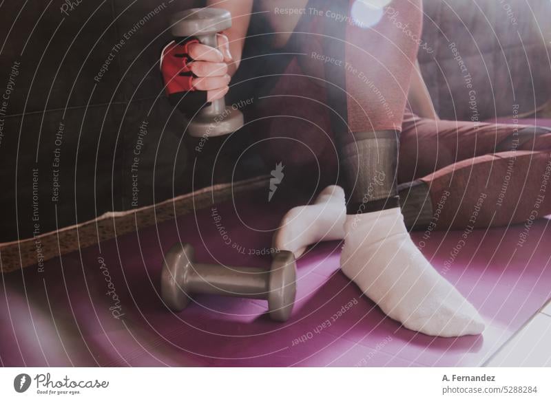 Detail of a woman holding a small dumbbell while exercising at home sitting on a yoga mat. Dumbbell Dumbbells dumbbell training exercise exercise mat exercised