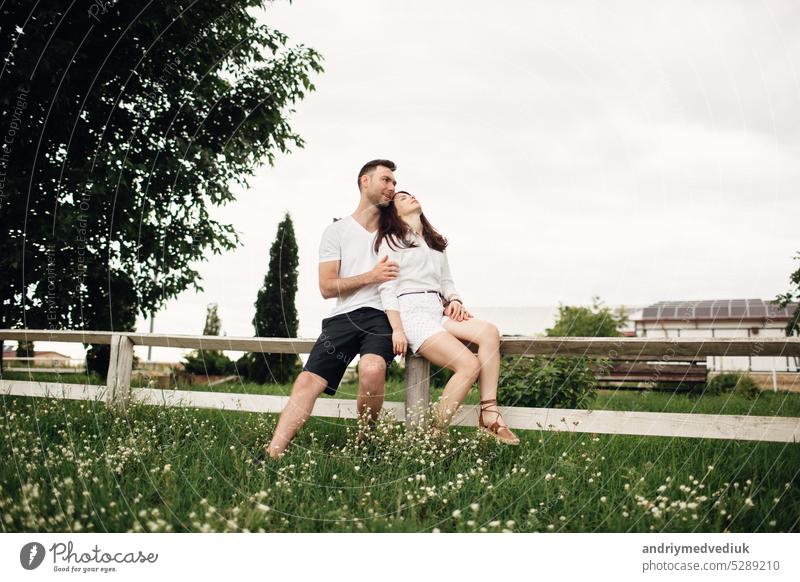 Loving couple is sitting in the summer park on white fence. man and woman are hugging outdoors on warm day adult young two together romantic relationship