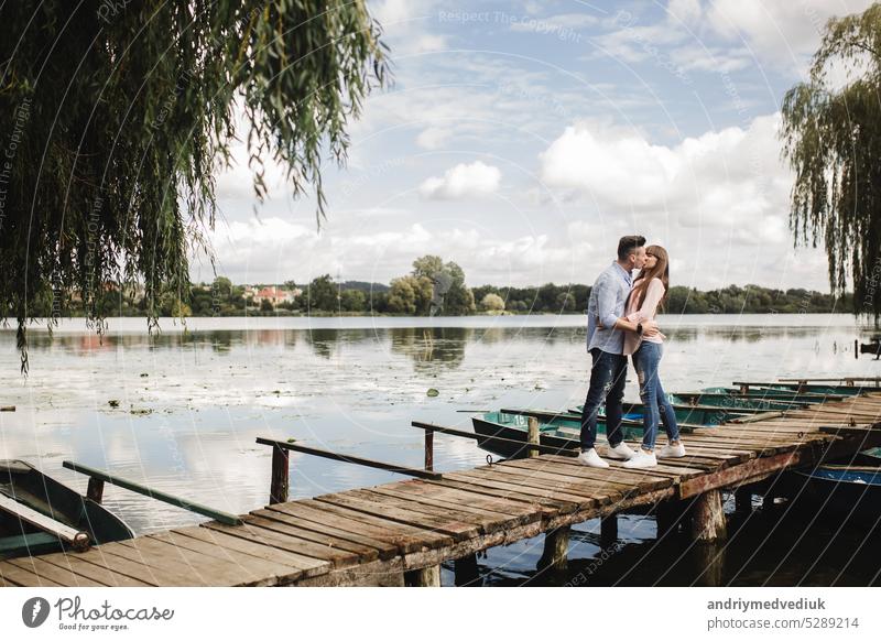 Young romantic couple is having fun in summer sunny day near the lake. Enjoying spending time together in holiday. Man and woman are hugging and kissing. happy