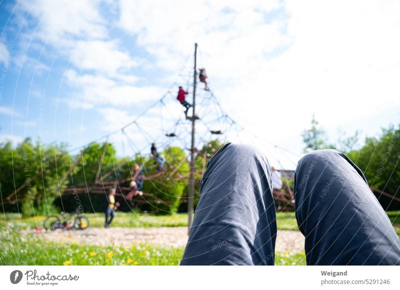 Legs of man lying on meadow in nice weather watching his children playing and climbing in background while he rests Break Playing Playground climbing scaffold