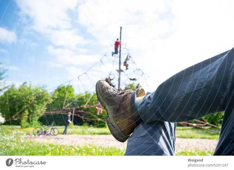 Crossed legs of a man lying on a meadow in nice weather watching his children playing and climbing in the background while he rests Break Playing Playground