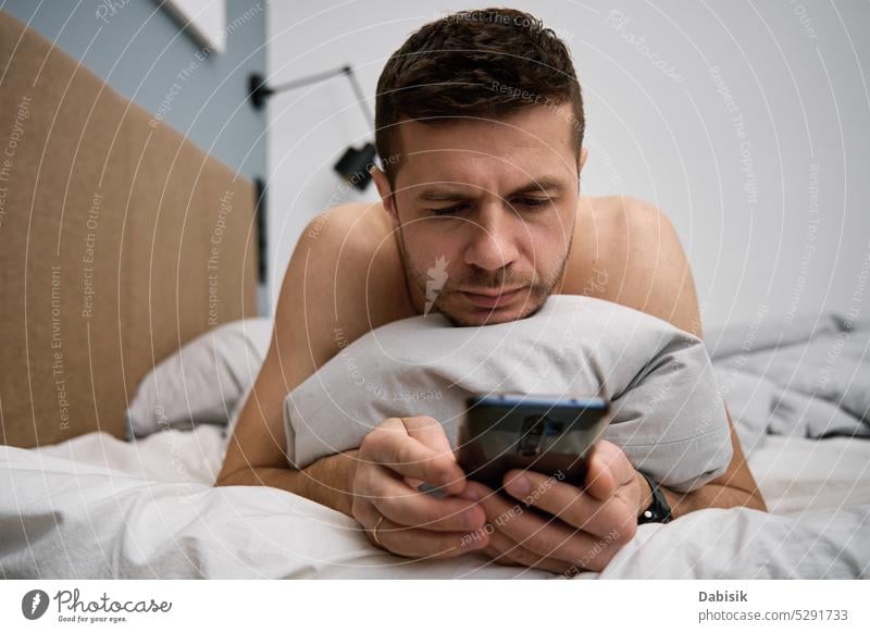 Phone addiction. Man lying in bed with smartphone man bedroom lifestyle browsing morning leisure cellphone online resting blanket technology home concept mobile