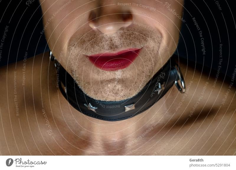 man in a BDSM collar smiles with his lips painted with red lipstick LGBT+ bdsm boy dark background gay gender grin human leather collar lgbt person low key
