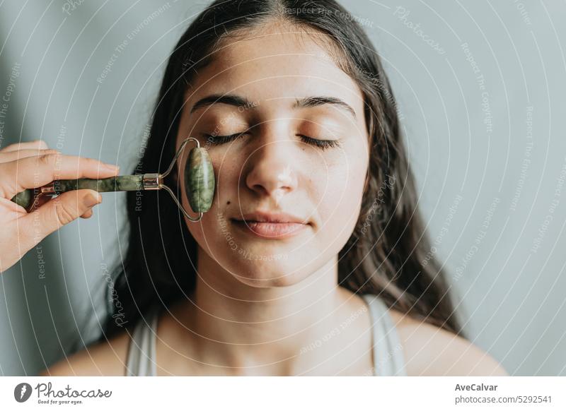 Happy young woman being treated her face with a quartz roller. Providing a variety of benefits for your skin health. Alternative anti-aging. tool care using