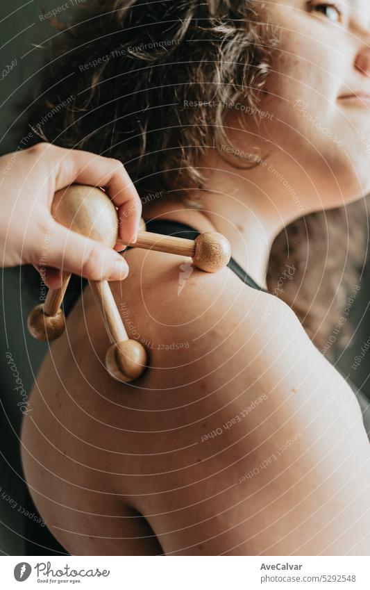 Hand holing a roller wooden skin massager in the back of model. Madero therapy massage with wooden rolling pin to stimulate the blood circulation. tool care