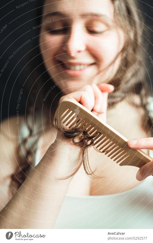 Cheerful woman grooming her hair with a wooden comb. Hair split ends treatment, daily rutine and rituals for perfect and glowing long hair. beauty personal care