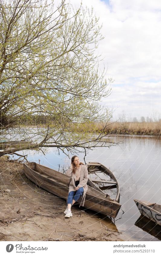 beautiful young woman is sitting and having fun in a boat near the river in spring day. background people loneliness human girl landscape female wood relaxation