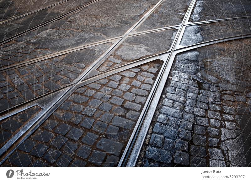 tramway railway crossing on a cobblestone street in lisbon Portugal, with some rain puddles, track junction, urban textures tracks streetcar train intersection