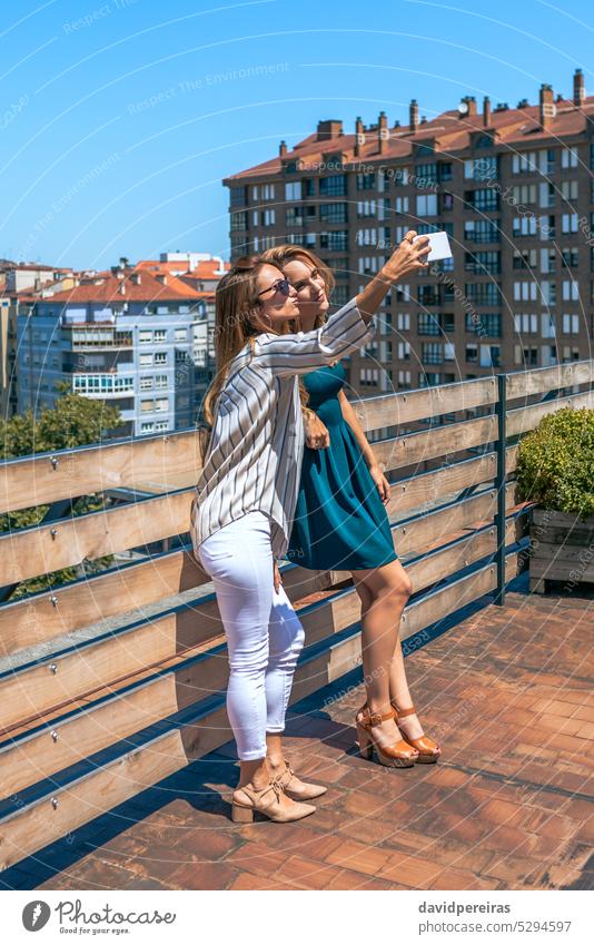 Two female friends taking a selfie in rooftop city on a summer day woman happy smile smiling photo terrace portrait phone friendly telephone looking mobile cell