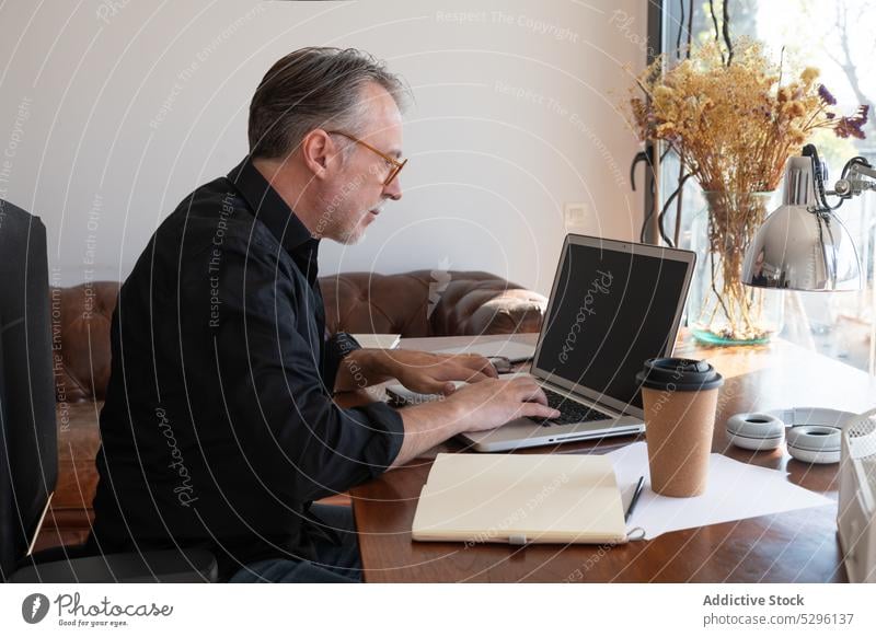 Man working on netbook at workplace freelance man using laptop home project living room interior comfort sunlight remote online business browsing device gadget