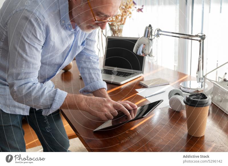 Serious man working on tablet at home entrepreneur freelance using digital office business remote browsing gadget device empty screen online desk internet focus