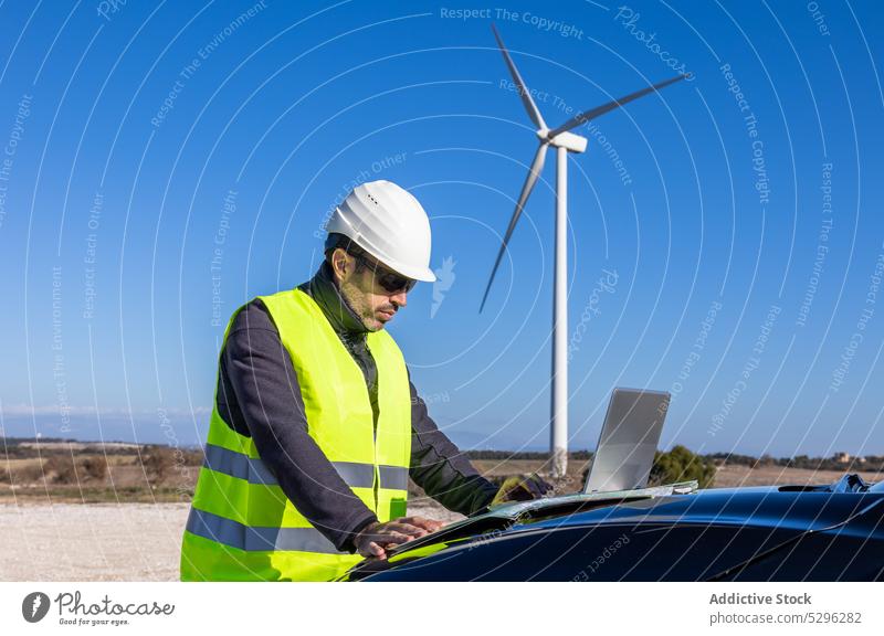 Male engineer examining map on hood of car man examine countryside worker wind turbine innovation power alternative energy cloudless sky sustainable propeller