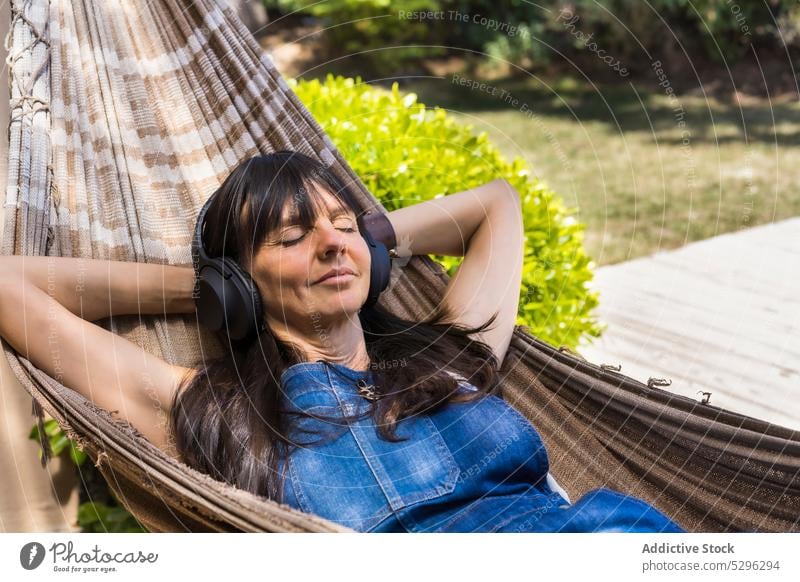 Happy woman listening to music in hammock in park headphones rest yard smile relax leisure song device happy enjoy delight casual audio wireless female positive