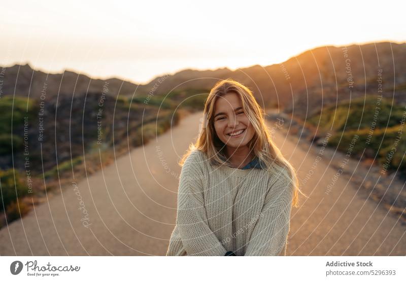 Smiling woman standing against mountains at sundown road sunset summer traveler picturesque leisure trip happy smile female freedom enjoy idyllic harmony