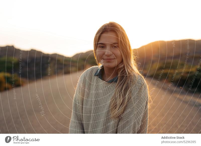 Smiling woman standing against mountains at sundown road sunset summer traveler picturesque leisure trip happy smile female freedom enjoy idyllic harmony