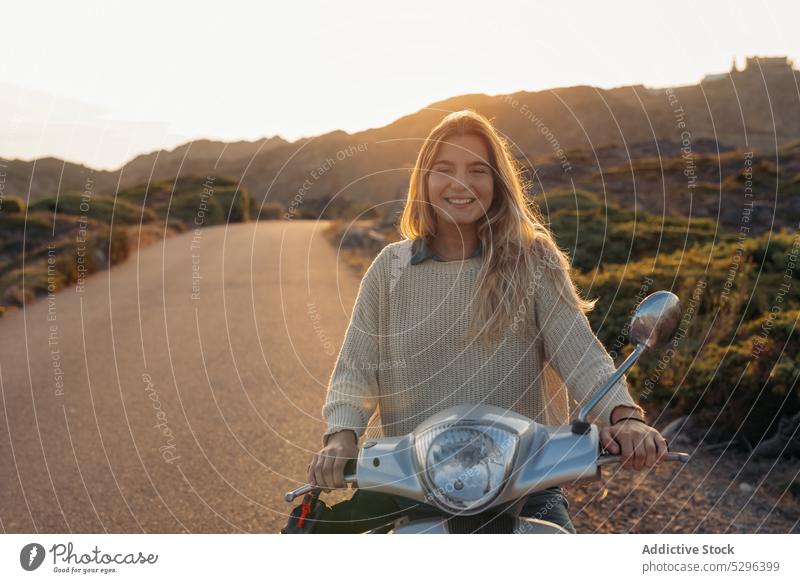 Young woman on scooter in countryside road trip vehicle weekend route travel sunset sundown mountain happy smile blond young female enjoy alone nature harmony