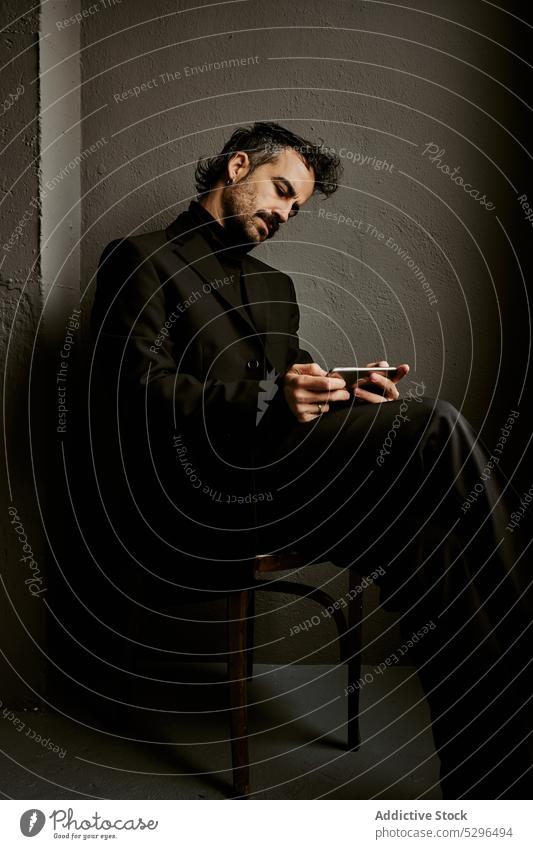 Confident man using smartphone in dark room browsing gadget chair thoughtful beard wireless gentleman serious adult male classy connection mobile online