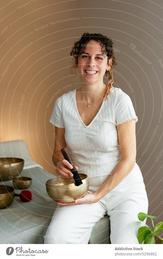 Cheerful woman with Tibetan singing bowl looking at camera in spa center portrait sound massage tibetan singing bowl positive therapist therapy relax music
