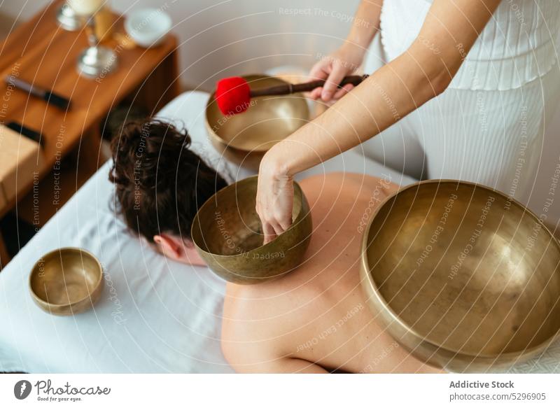 Crop female playing singing bowl placed on back of female client during meditation women meditate zen music recreation stress relief harmony melody sound