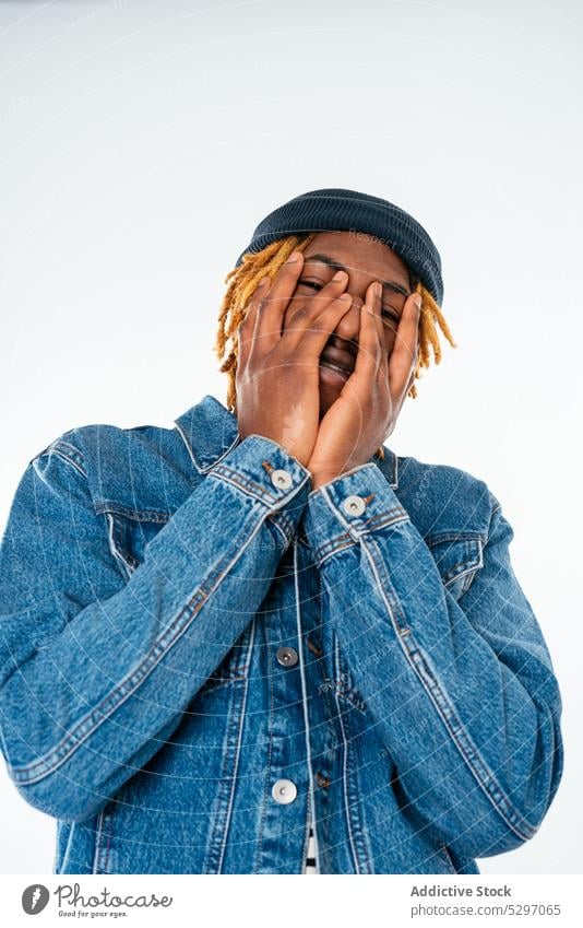 Cheerful black man in denim jacket laugh cheerful street style dreadlocks facepalm cover face gesture hairstyle studio shot happy casual smile fun male positive