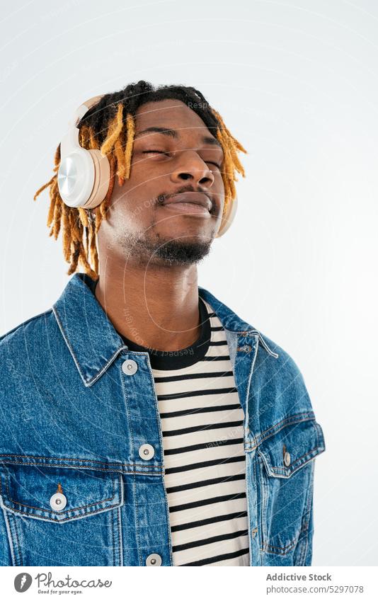 Black man listening to music in headphones positive enjoy pleasure casual studio shot wireless male dreadlocks african american ethnic black gadget modern denim