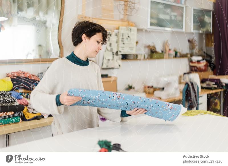 Focused tailor with roll fabric in atelier woman sew seamstress dressmaker workshop creative examine concentrate focus designer busy occupation female studio