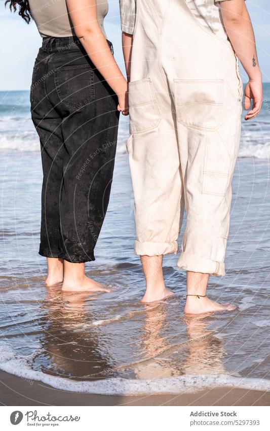 Crop lesbian couple holding hands while standing in sea water date in love lgbt happy young fun girlfriend having fun together freedom spend time gentle ocean