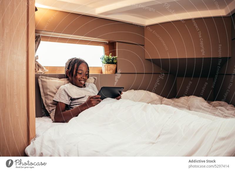 Cheerful black boy browsing tablet in bed using internet surfing online glad lying connection gadget device african american comfort positive ethnic free time