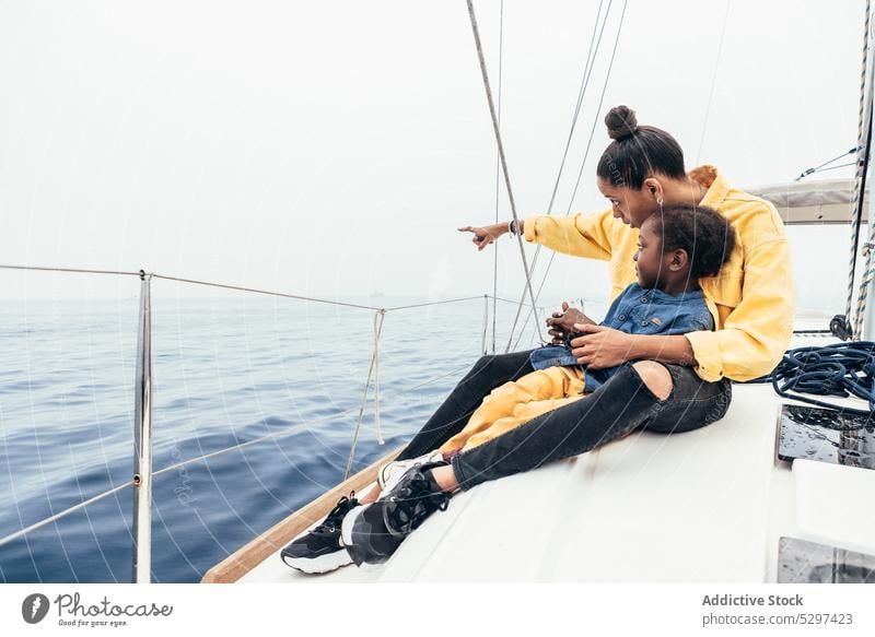 Cheerful black woman showing view to boy mother son point away yacht smile together weekend happy demonstrate child casual gesture sea summer parent kid