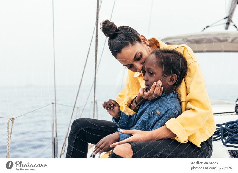 Cheerful black woman embracing son in yacht mother smile together weekend hug embrace happy boy child casual gesture sea summer parent kid glad affection