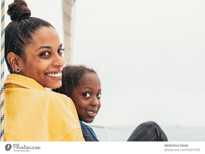 Cheerful black woman embracing son in yacht mother smile together weekend hug embrace happy boy child gesture sea summer parent kid glad affection adorable