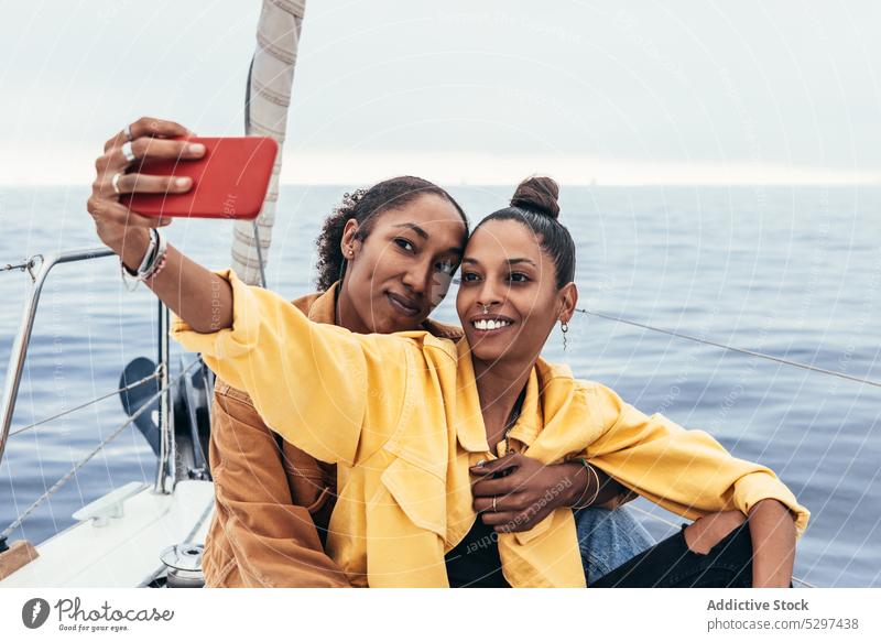 Cheerful black girlfriends taking selfie on yacht women smartphone smile hug relationship together couple happy embrace ethnic device gadget african american