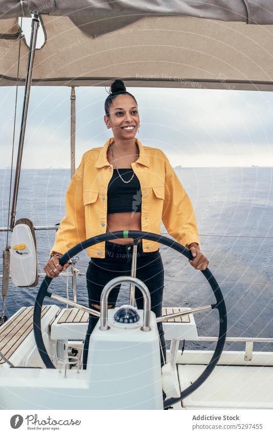 Cheerful black woman standing at steering wheel of yacht sea smile summer style trip travel sailboat female happy african american jacket positive water