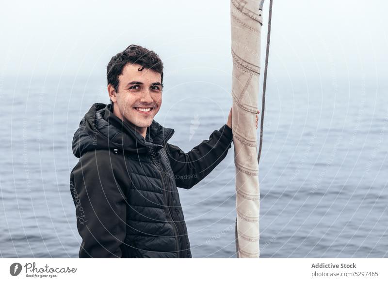 Cheerful man standing near sail on yacht sea water smile trip tourist sailboat cruise male outerwear happy travel traveler vacation ocean journey cheerful