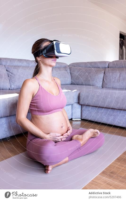 Pregnant woman in VR headset meditating on floor yoga meditate lotus pose padmasana vr home pregnant practice female virtual reality wellness focus concentrated